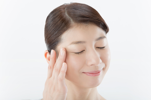 目を閉じて目元を触っている女性