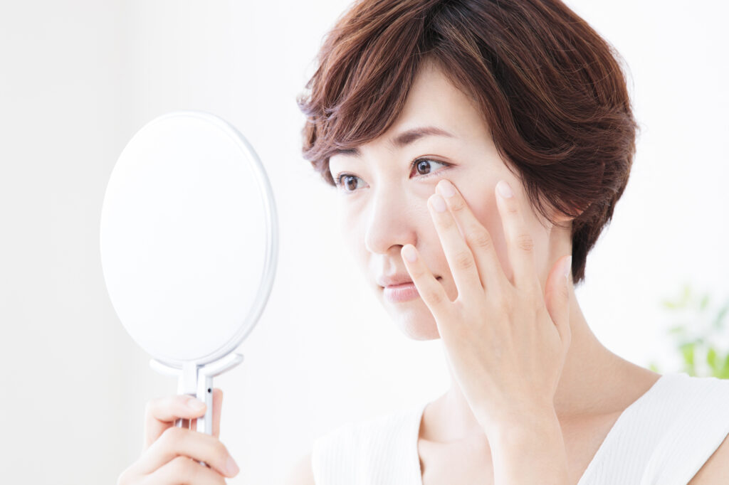 鏡を見ながら、目の下を触ったいる女性